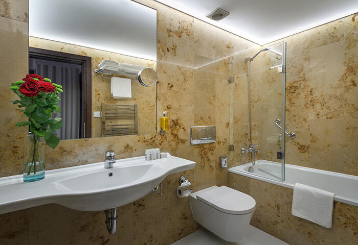 Hotel Clementin Old Town bathroom. Modern design with marble walls, a bathtub with glass screen, and a bouquet of red roses. Gay Prague hotel.