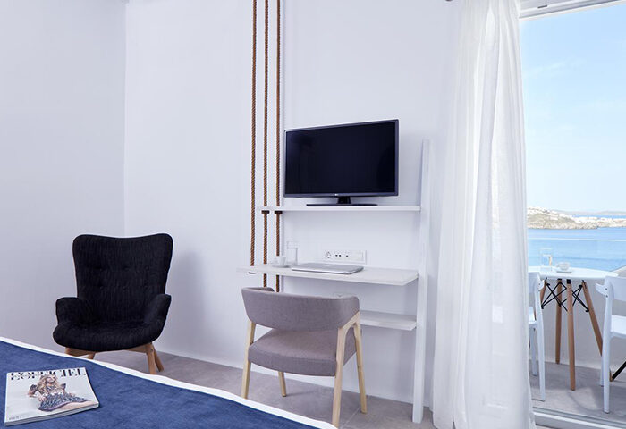 Mykonos Town suite's interior at Absolute Mykonos Suites & More, a luxury gay hotel. Features a private balcony with ocean views, TV, and desk.