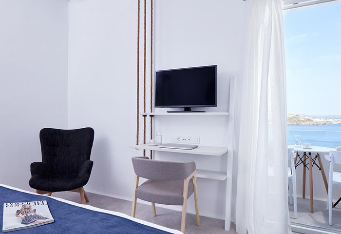 Mykonos Town suite's interior at Absolute Mykonos Suites & More, a luxury gay hotel. Features a private balcony with ocean views, TV, and desk.