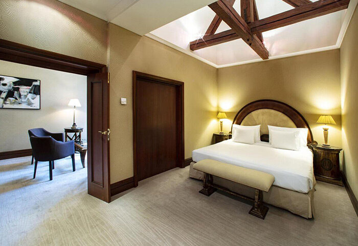 NH Collection Carlo IV hotel room. Luxury gay hotels in Prague at cheap price. Bedroom with double bed, bench, and seating area.