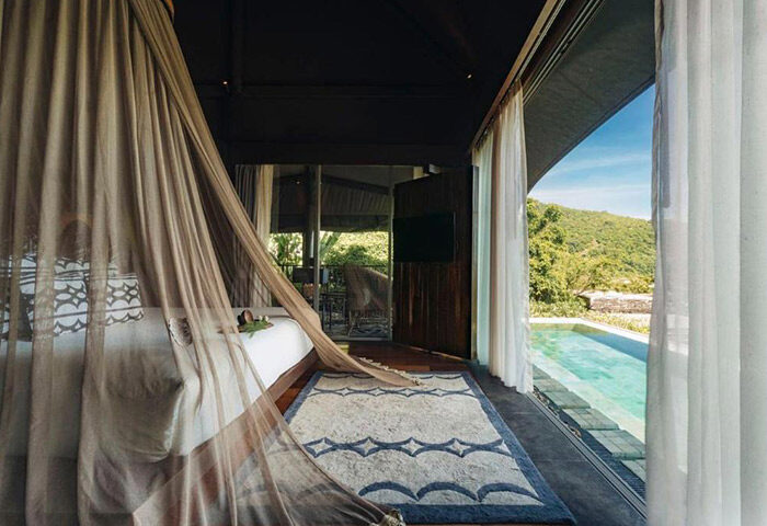 Keemala Phuket luxury private pool villa. Gay hotel room interior with canopy bed, rug, and view of pool and tropical landscape.