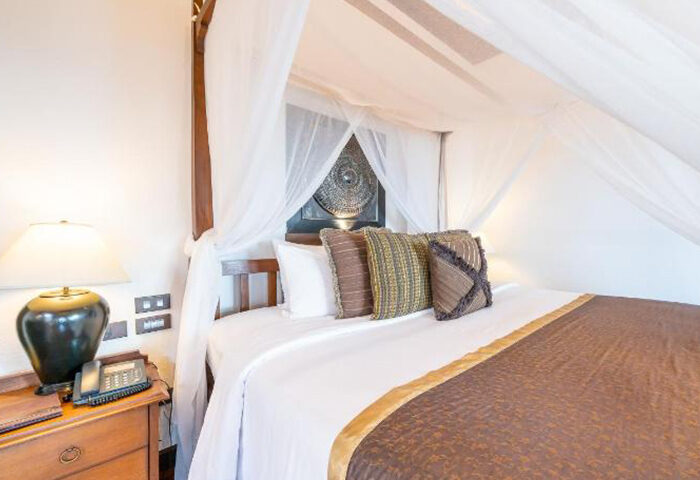 Le Vimarn Cottages & Spa beachfront hotel room. Canopy bed with decorative pillows. Gay travel Koh Samet hotel room. Find cheap hotels now.