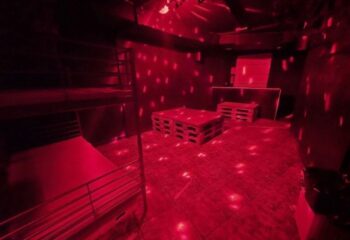 Inside Firewood Madrid, a gay cruise club: Red lighting, pallet tables, and a bunk bed create a unique, intimate space for gay men's travel.