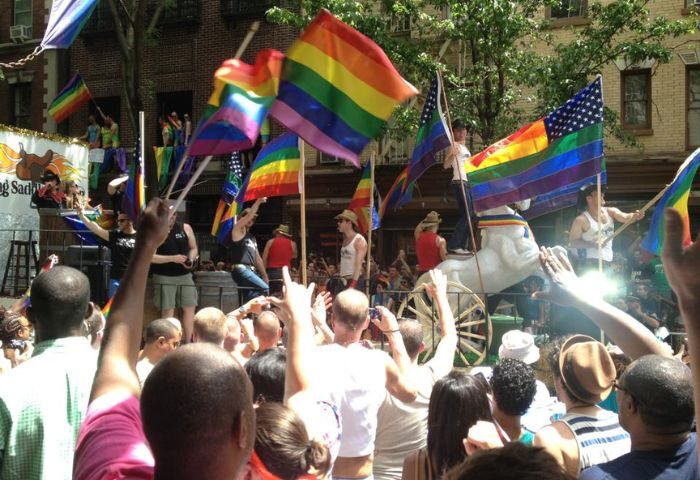 NYC gay pride parade featuring the Flaming Saddles gay bar float. Rainbow flags and cheering crowds celebrate LGBTQ+ travel in New York.