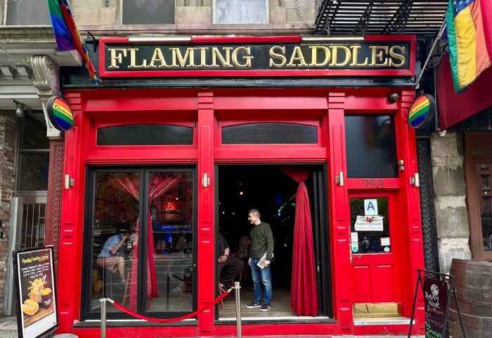Flaming Saddles gay bar in New York City. Red facade with rainbow flags. Gay travel destination, popular nightlife spot.
