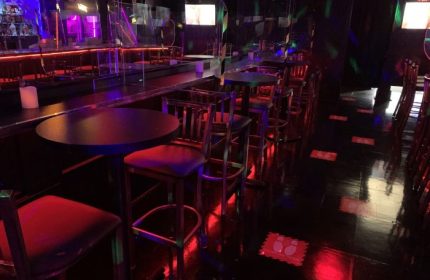 Interior of Flash on Church, a gay bar in Toronto. Tables and chairs line the dance floor. Red and purple lighting. Gay travel.