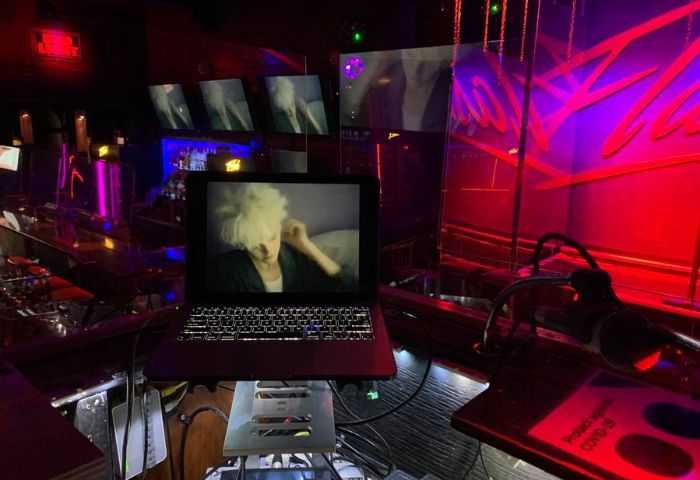 Inside Flash on Church, a Toronto gay bar. A laptop displays a performer. The bar features colorful lighting and screens. Nightlife scene.