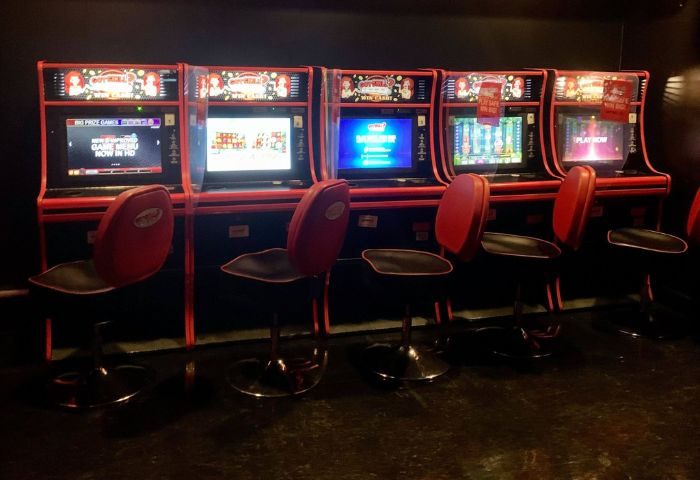 Slot machines line a wall at Flash on Church, a gay bar in Toronto. Red stools sit in front of each machine.