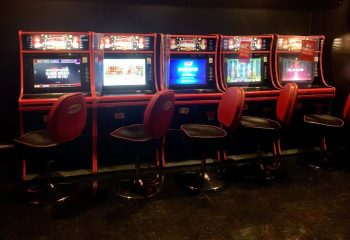 Slot machines line a wall at Flash on Church, a gay bar in Toronto. Red stools sit in front of each machine.