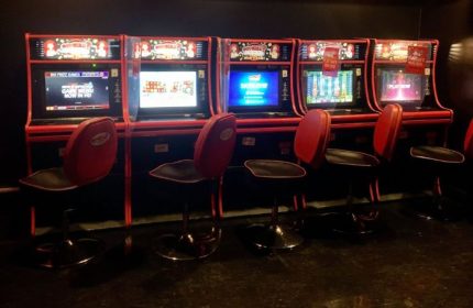 Slot machines line a wall at Flash on Church, a gay bar in Toronto. Red stools sit in front of each machine.