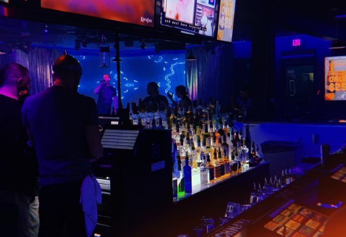 Flex Cocktail Lounge in Las Vegas. Interior view of the bar area with bottles, screens, and people in a dimly lit, blue-toned space.