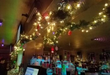 Festive decor at Flux Bar. Garland and lights adorn the bar area, creating a warm ambiance. A gay bar known for its dancefloor and vibrant atmosphere.