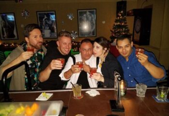 Five people at Flux Bar having fun, raising glasses. Gay travel advice, nightlife. Christmas tree in background.