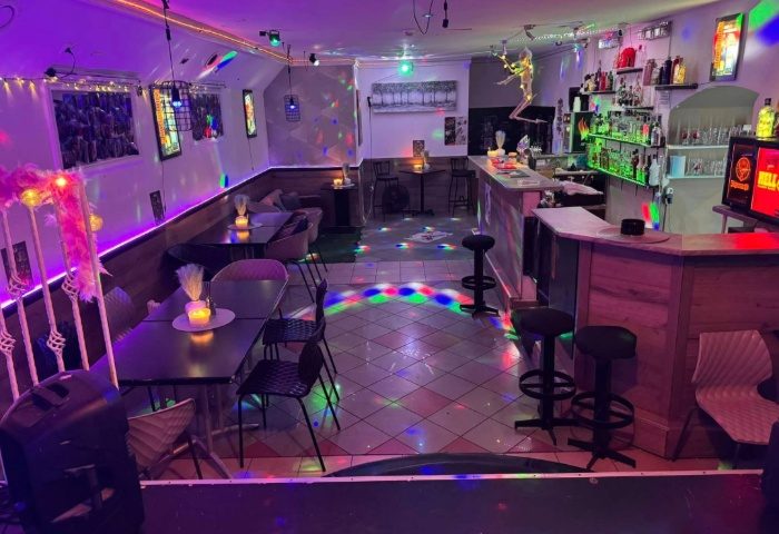 Interior of Freedom Club, Budapest, a gay bar with colorful lighting, tables, chairs, bar stools, and a well-stocked bar for gay men travel.