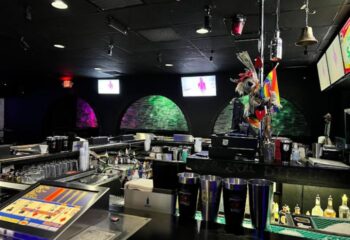 Freezone Gay Bar in Las Vegas interior. Black ceiling, arched alcoves with colored lights, bar with bottles, glasses, and a video poker machine.