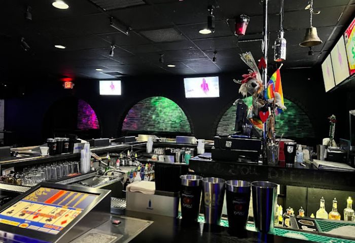 Freezone Gay Bar in Las Vegas interior. Black ceiling, arched alcoves with colored lights, bar with bottles, glasses, and a video poker machine.