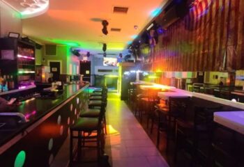Friend's Tavern, a gay bar in New York. Interior view of the bar with colorful lights, bar stools, and a dance floor. Gay travel advice.