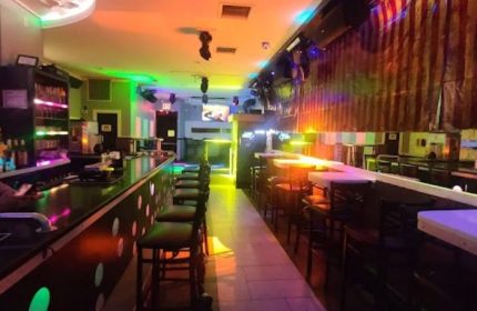 Friend's Tavern, a gay bar in New York. Interior view of the bar with colorful lights, bar stools, and a dance floor. Gay travel advice.