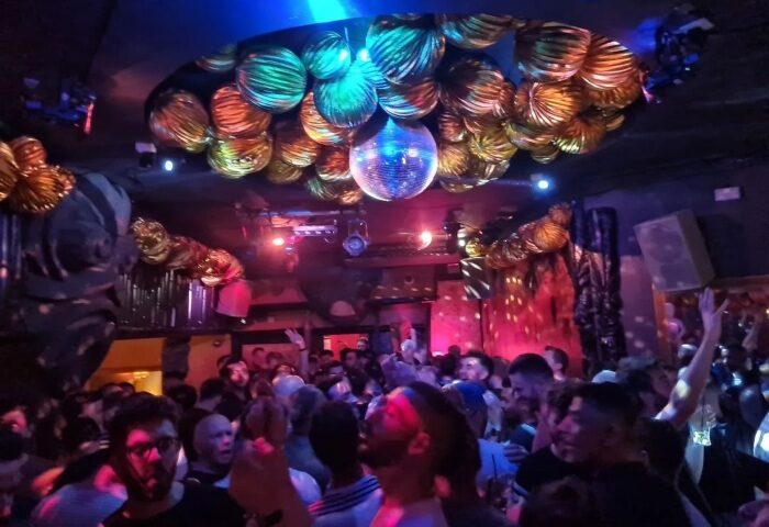 The Cock Tavern, London: Fun gay bar with dance floor. Crowd of men under disco ball and decorative orbs. Gay travel advice.