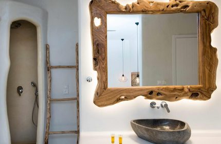 Unique bathroom design at Sahas Suites, a gay hotel in Mykonos. Features a stone sink, driftwood ladder, & rustic wood-framed mirror.