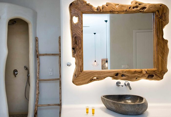 Unique bathroom design at Sahas Suites, a gay hotel in Mykonos. Features a stone sink, driftwood ladder, & rustic wood-framed mirror.