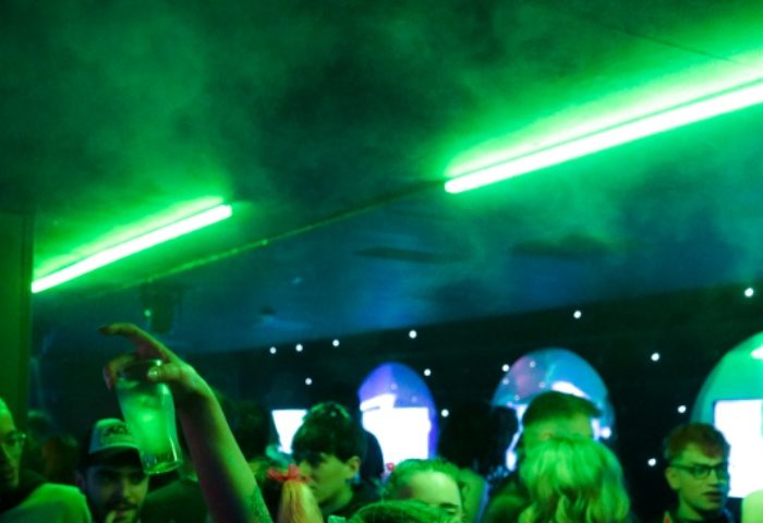 G-A-Y Manchester club scene. Crowd of people under green lights, one raising a drink. Gay travel advice for Manchester nightlife.