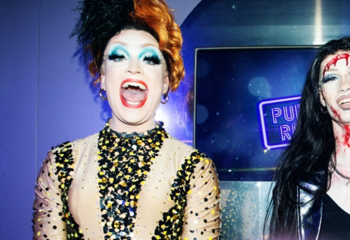 Drag queens at G-A-Y Manchester, a gay bar. Performers with dramatic makeup and costumes pose in front of a neon sign. Nightlife scene.