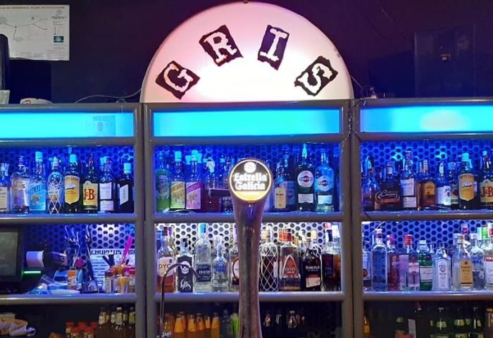 GRIS Gay Bar in Madrid: Well-stocked bar with blue lighting. GRIS sign above shelves of liquor bottles, Estrella Galicia tap in front.