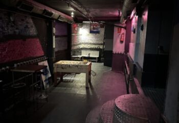 Interior of GRIS Gay Bar in Madrid, featuring a foosball table, exposed brick, and industrial design elements. Nightlife travel.