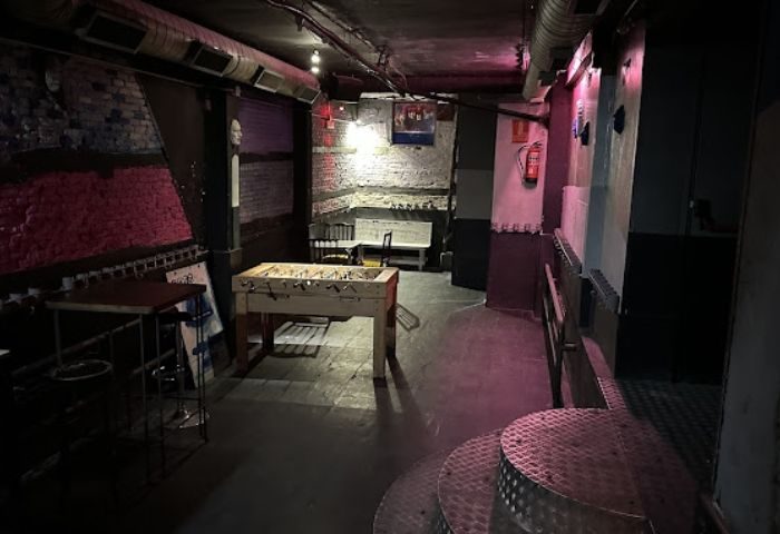 Interior of GRIS Gay Bar in Madrid, featuring a foosball table, exposed brick, and industrial design elements. Nightlife travel.