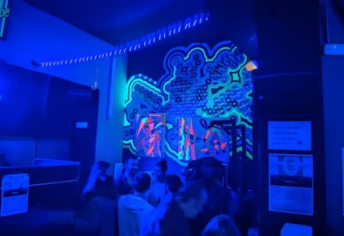 Interior of GRIS Gay Bar in Madrid, Spain. People gather under neon art and blue lights, enjoying the atmosphere of a popular gay nightlife spot.