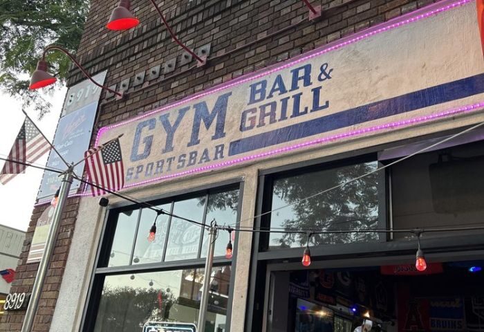 GYM Sportsbar banner. Exterior shot of the gay sports bar and grill. Flags, lights, and the GYM sign are visible. Gay travel destination.