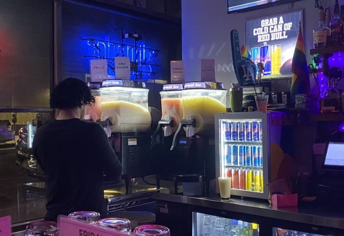 GYM Sportsbar drinks. Frozen cocktail dispensers at a gay bar. Red Bull cooler, LA Dodgers hand with rainbow flag, and rainbow flag on shelf.