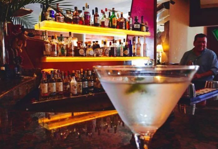 Martini at Garbo Piano Bar, gay live music venue in Puerto Vallarta. Shelves of liquor bottles behind the bar. Gay travel advice.
