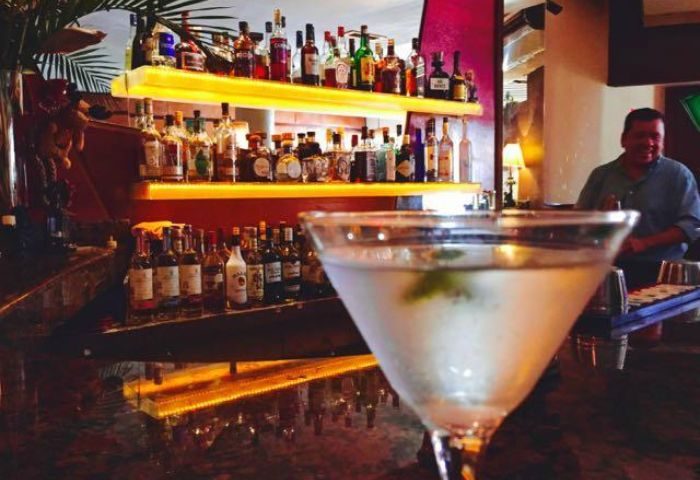 Martini at Garbo Piano Bar, gay live music venue in Puerto Vallarta. Shelves of liquor bottles behind the bar. Gay travel advice.