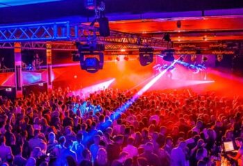 Garcons Budapest event: A large crowd of gay men party under blue & red lights. Stage lighting rig overhead. Budapest gay nightlife.