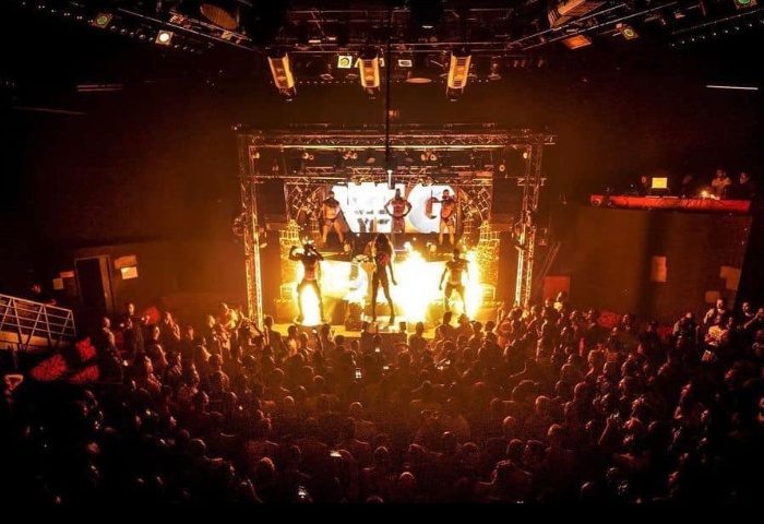 Milan Gate Party: Crowd watches stage performers at a gay dance club. Nightlife scene with dancers and stage lighting.