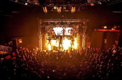 Milan Gate Party: Crowd watches stage performers at a gay dance club. Nightlife scene with dancers and stage lighting.