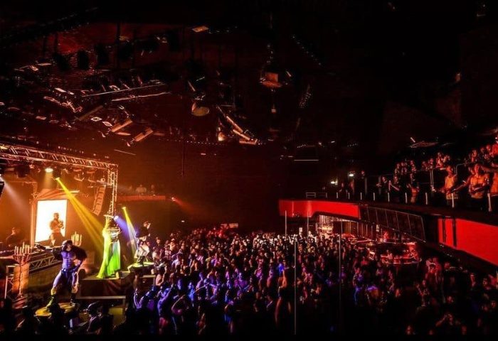 Packed Gate Party in Milan. Performers on stage entertain a large crowd at this gay nightlife event. Balcony seating visible.