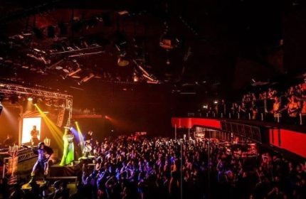 Packed Gate Party in Milan. Performers on stage entertain a large crowd at this gay nightlife event. Balcony seating visible.