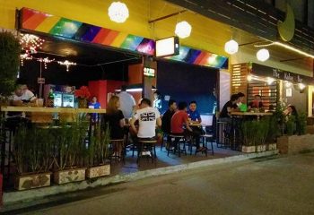 Gay bar street in Chiang Mai, Thailand. Soi Chareonprathet 6 night scene with people at outdoor tables under rainbow awning.