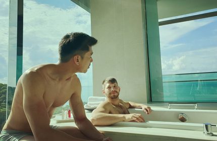 Gay honeymoon couple at Rayong Marriott Resort & Spa. Two men relax in a luxurious bathroom with ocean views. Perfect gay beach hotel.