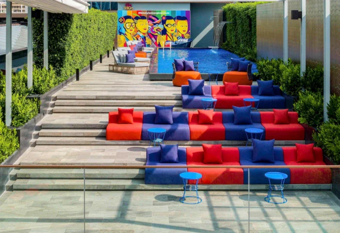 Ibis Styles Bangkok Silom's stylish pool area. Colorful seating tiers, lush greenery, and a vibrant mural create a gay-friendly, budget-chic vibe.