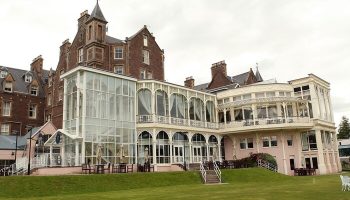 Crieff Hydro, a gay-friendly hotel. Exterior view of the hotel with its glass-enclosed structures and well-manicured lawn. Travel advice.