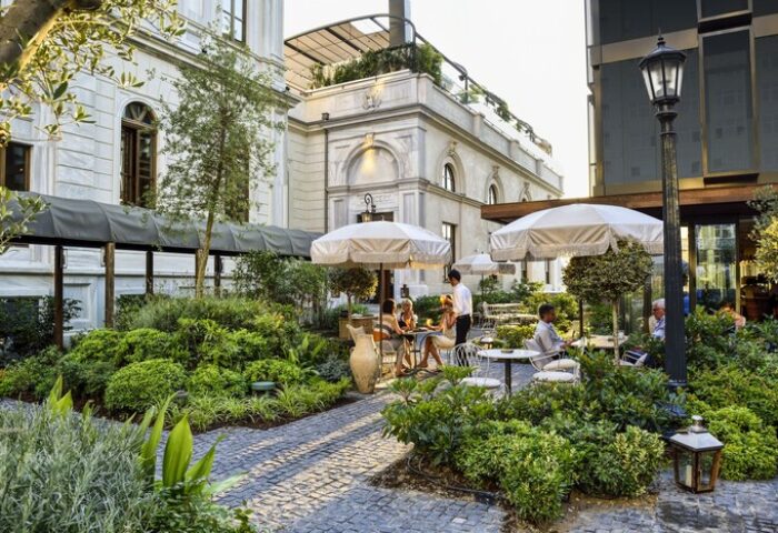 Soho House Istanbul's gay-friendly hotel garden. Outdoor seating, umbrellas, and lush greenery create a relaxing atmosphere. Ideal for gay travelers.
