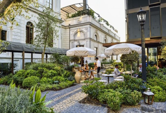 Soho House Istanbul's gay-friendly hotel garden. Outdoor seating, umbrellas, and lush greenery create a relaxing atmosphere. Ideal for gay travelers.