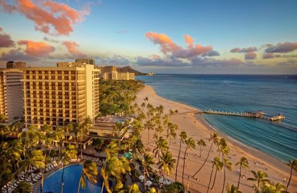 Hilton Hawaiian Village Waikiki Beach Resort, a gay-friendly hotel. Beachfront view with palm trees, ocean, and Diamond Head in the distance.