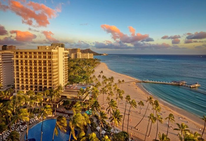 Hilton Hawaiian Village Waikiki Beach Resort, a gay-friendly hotel. Beachfront view with palm trees, ocean, and Diamond Head in the distance.