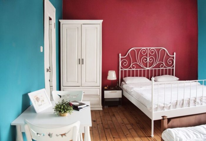 Cheers Midtown Hostel gay-friendly hotel room. Red accent wall, white bed, wardrobe, desk and chairs. Modern, clean, and inviting space.