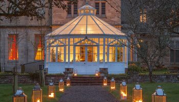 Schloss Roxburghe Hotel's gay-friendly charm. Lantern-lit path leads to a glass conservatory, promising a welcoming escape for gay travelers.